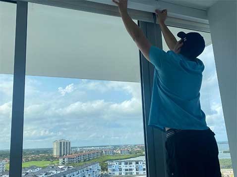 A man putting up shades on a large window overlooking