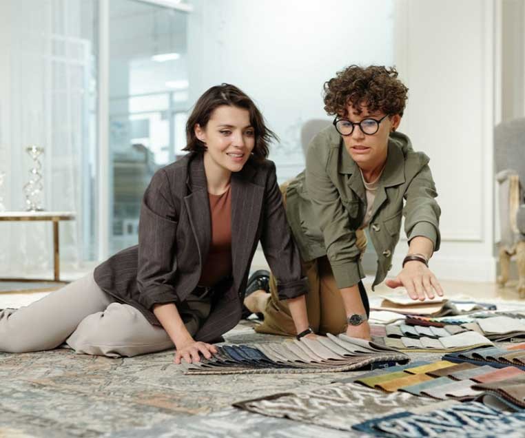 Two women crouched on the floor, looking at fabric samples